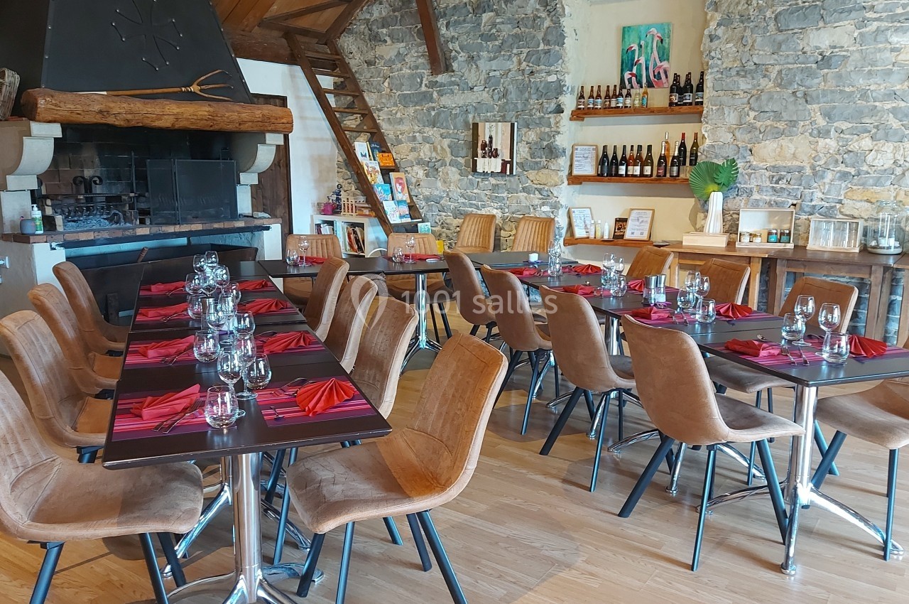 Salle de restaurant avec tables dressées, chaises en cuir, murs en pierre et cheminée décorative.