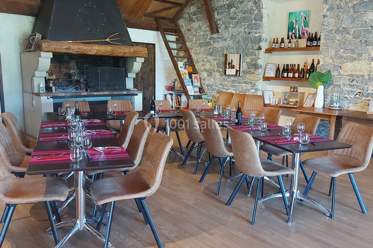 Salle de restaurant avec tables dressées, chaises en cuir, cheminée en pierre et étagères garnies de bouteilles.