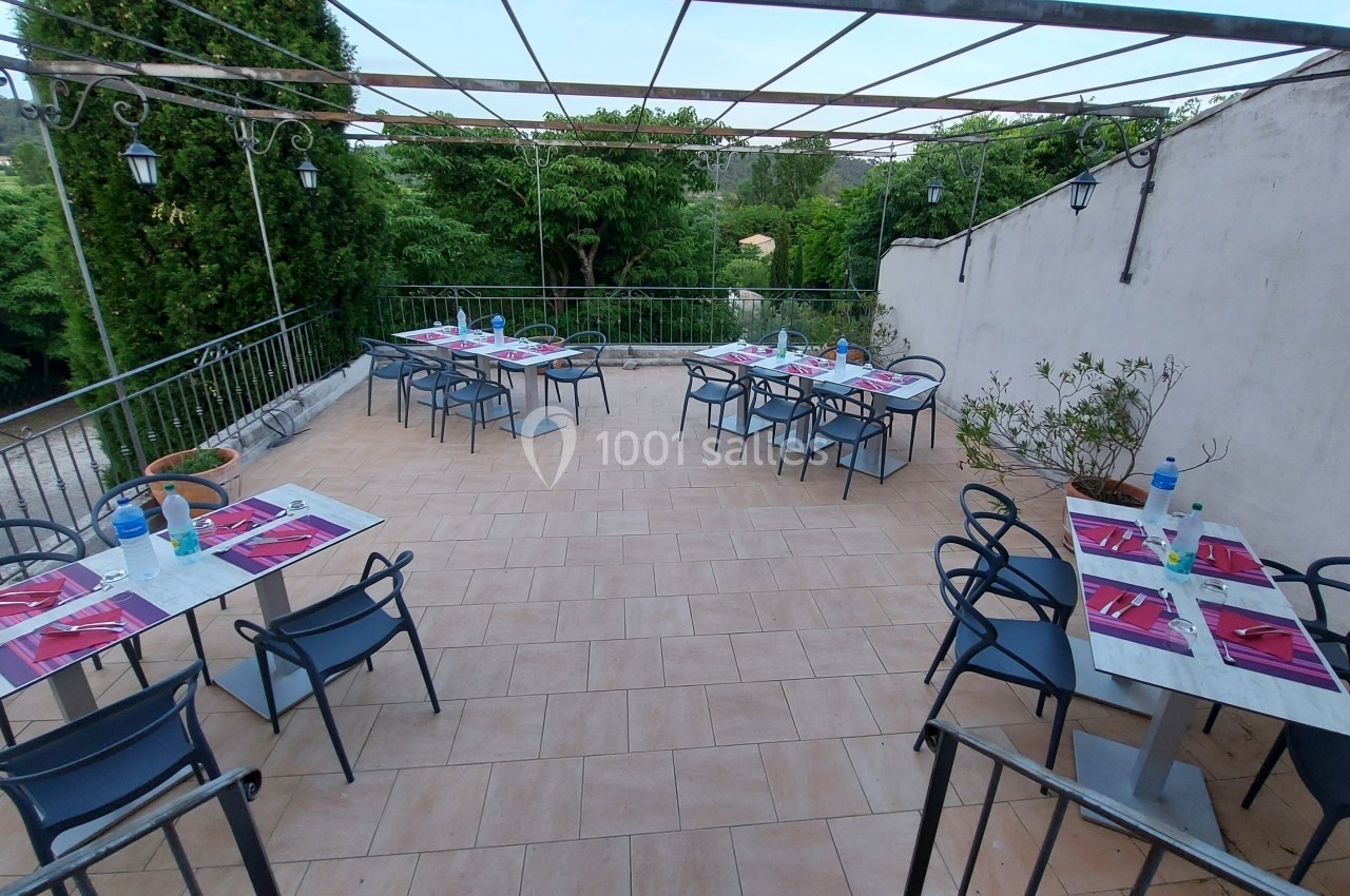 Terrasse extérieure avec tables dressées, chaises noires et vue sur des arbres et collines verdoyantes.