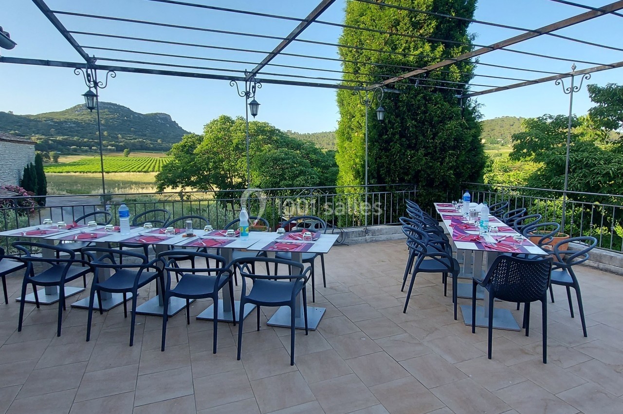 Terrasse aménagée avec deux grandes tables dressées, entourée de verdure et offrant une vue sur des collines.