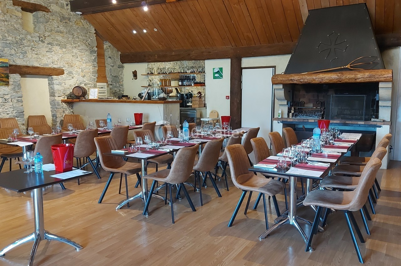 Salle de restaurant avec tables dressées, chaises en bois, cheminée en pierre et décor rustique.