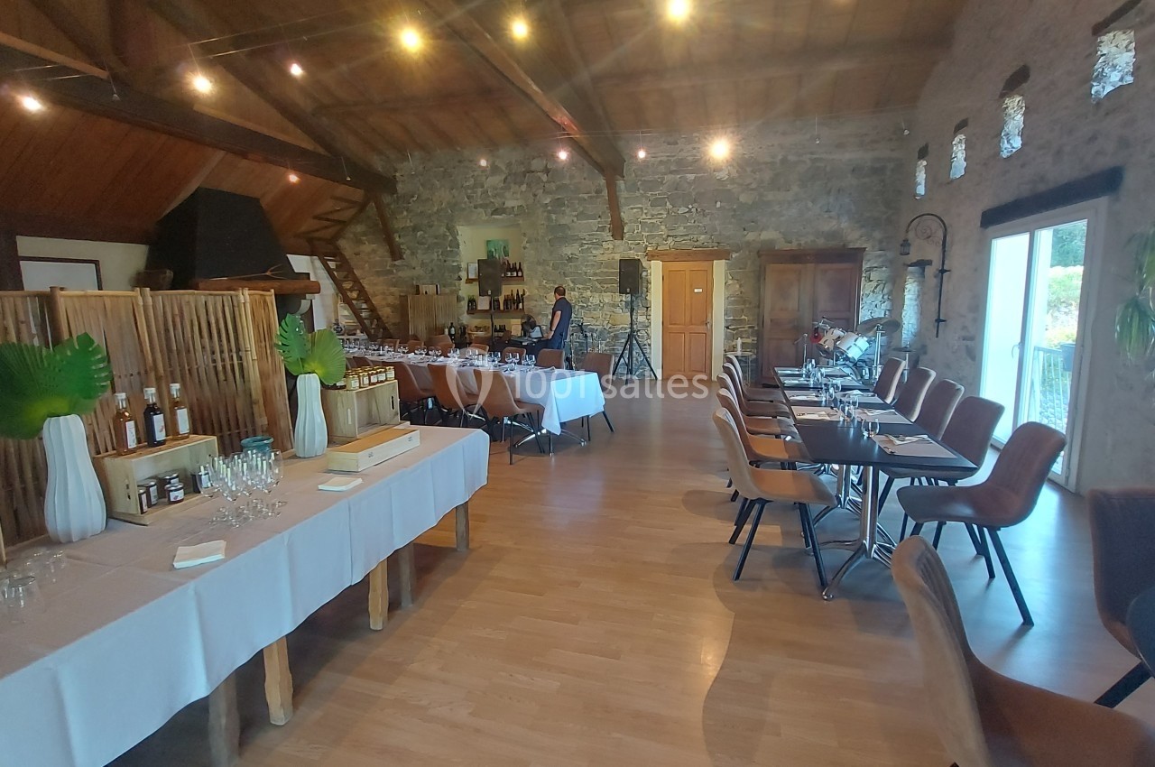 Salle de réception lumineuse avec tables dressées, murs en pierre apparente et plafond en bois.