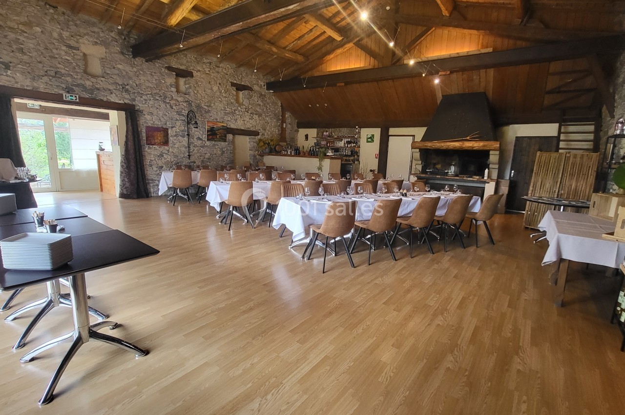 Salle de réception avec tables dressées, chaises en bois, murs en pierre et plafond en bois, éclairée par des lumières et…