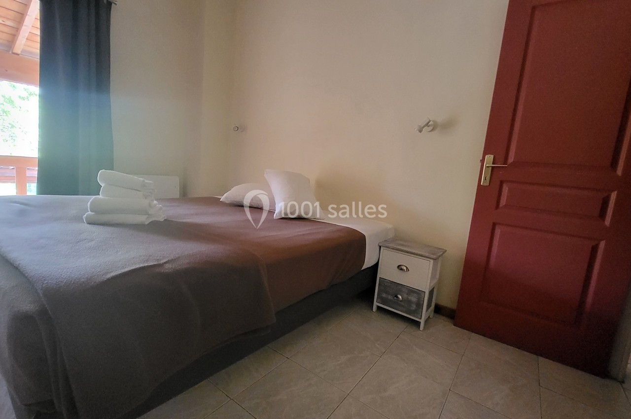 Chambre lumineuse avec lit double, draps bruns, serviettes pliées, table de chevet et porte rouge.