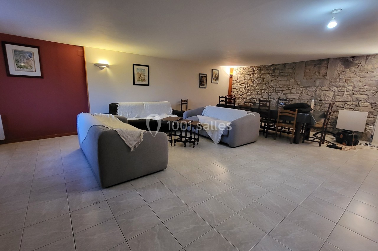 Salle spacieuse avec canapés recouverts de plaids, tables et chaises en bois, mur en pierre et éclairage doux.