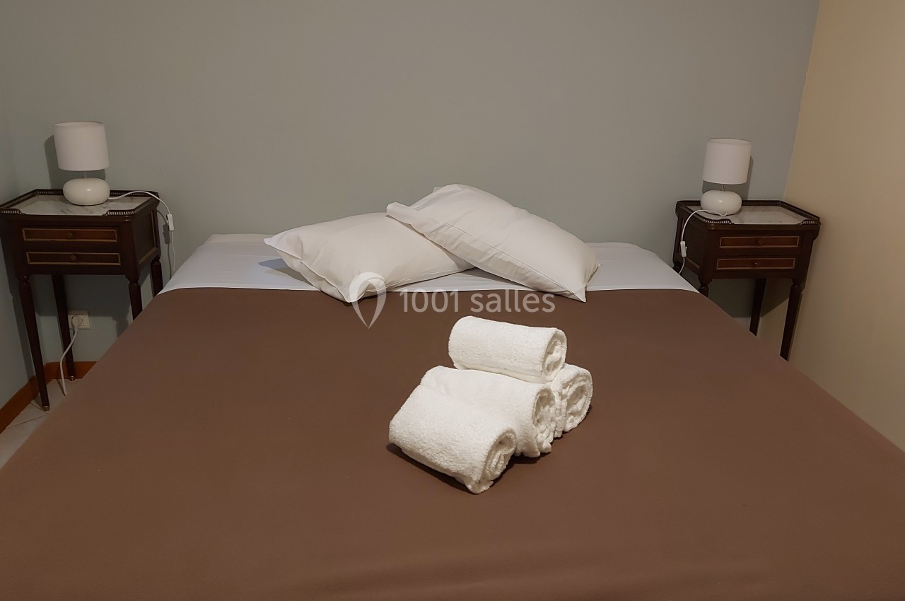 Lit double avec couvre-lit marron, oreillers blancs et trois serviettes roulées posées au centre, deux lampes de chevet.