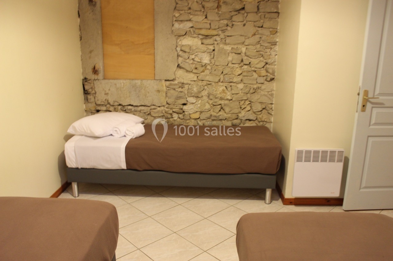 Chambre avec lits simples, murs en pierre apparente et carrelage au sol, éclairée par une lumière douce.