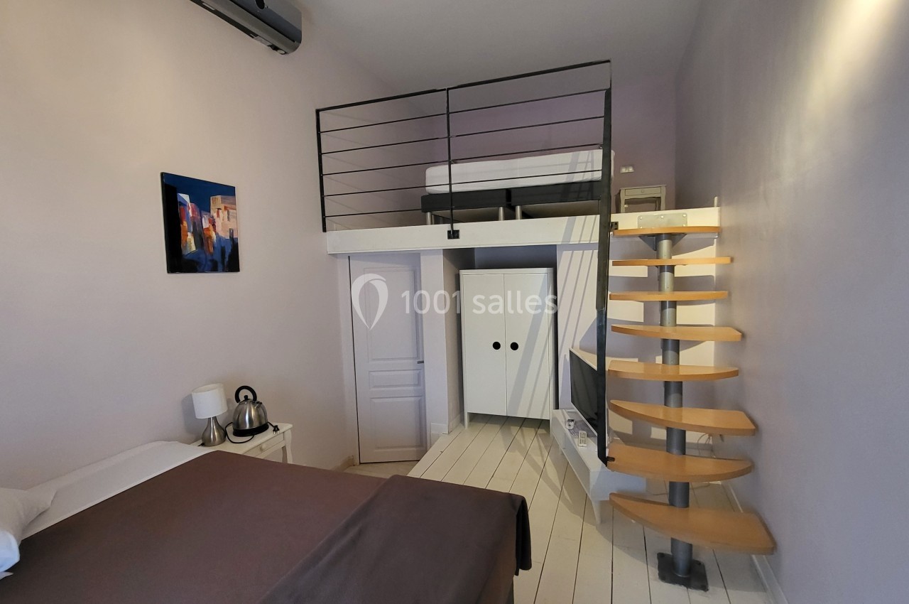 Chambre avec lit double, mezzanine, escalier en colimaçon, armoire blanche et décoration murale colorée.