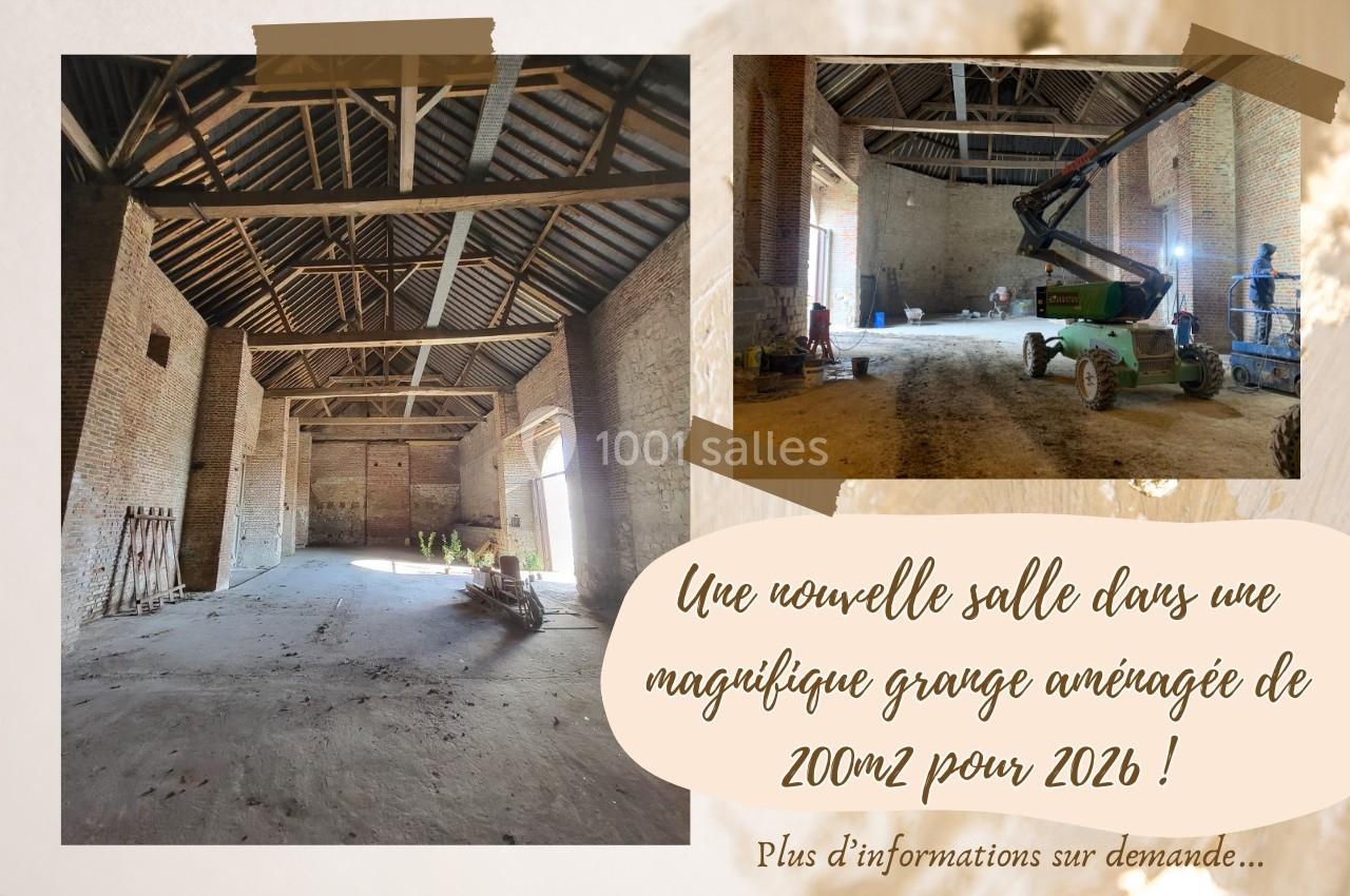 Intérieur d'une grande grange en rénovation avec des murs en briques, une charpente apparente et une nacelle élévatrice.