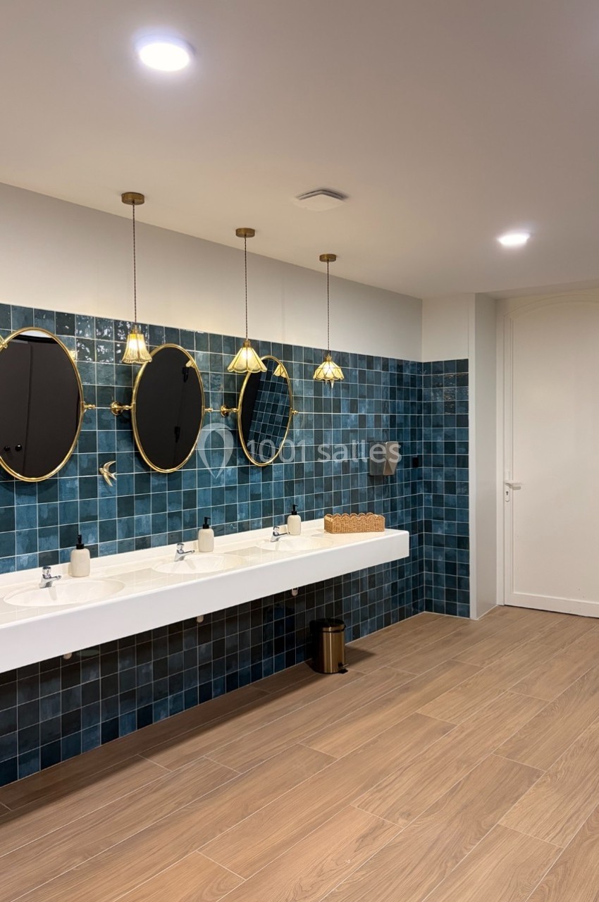 Salle de bain moderne avec carrelage bleu, trois miroirs ronds, un plan vasque blanc et un sol en bois clair.