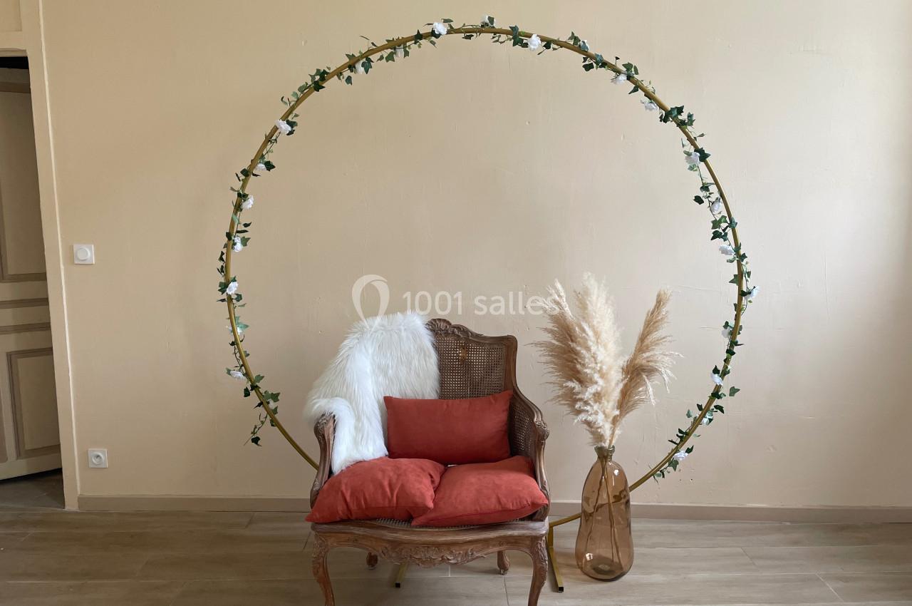 Fauteuil en osier avec coussins rouges, décoré d'un cercle floral et d'un vase contenant des herbes séchées.