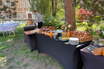 Miniature Brunch dans la cour intérieure du Château Pièce rustique avec murs en pierre, plafond en bois, réservoir métallique rouge et mobilier simple.