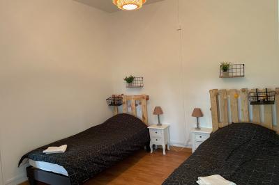 Miniature Chambre avec 2 lits simples Pièce rustique avec murs en pierre, plafond en bois, réservoir métallique rouge et mobilier simple.