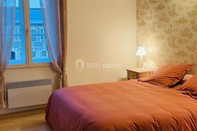 Miniature Chambre nuptiale du gîte Pièce rustique avec murs en pierre, plafond en bois, réservoir métallique rouge et mobilier simple.