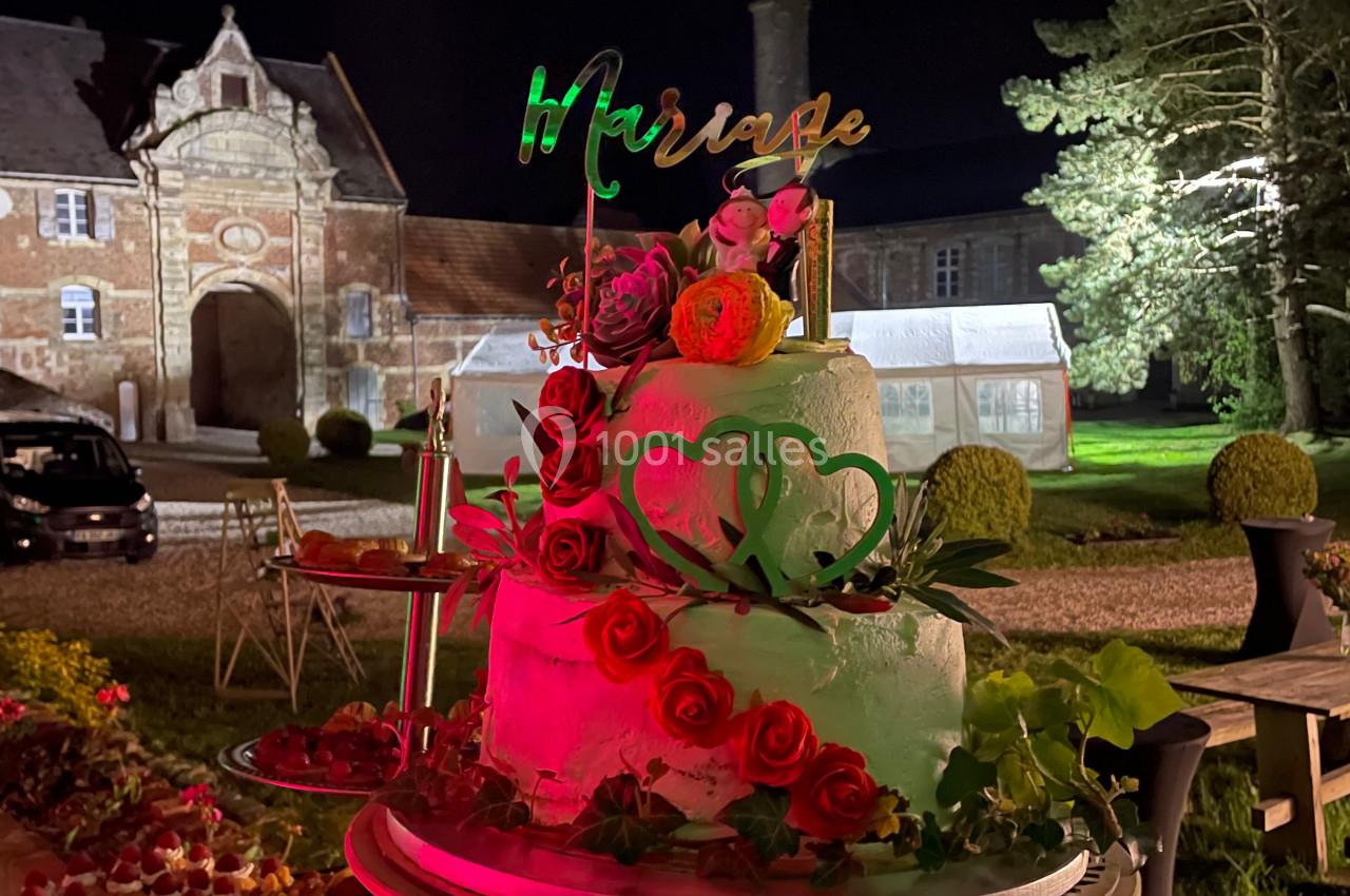 Gâteau de mariage décoré de roses rouges et blanches, posé sur une table en extérieur devant un bâtiment éclairé la nuit.
