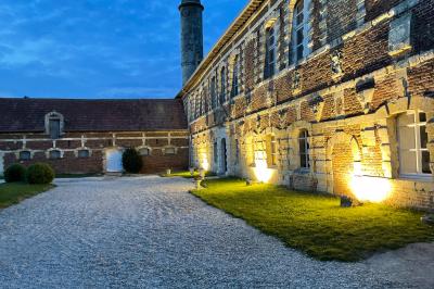 Miniature Cour intérieure éclairée du Château Pièce rustique avec murs en pierre, plafond en bois, réservoir métallique rouge et mobilier simple.