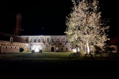 Miniature Cour intérieure éclairée du Château Pièce rustique avec murs en pierre, plafond en bois, réservoir métallique rouge et mobilier simple.