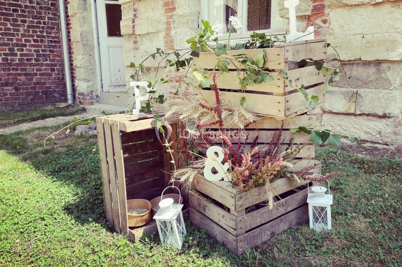 Cagettes en bois empilées avec des plantes, décorées de lettres blanches et lanternes, sur une pelouse devant un mur en…