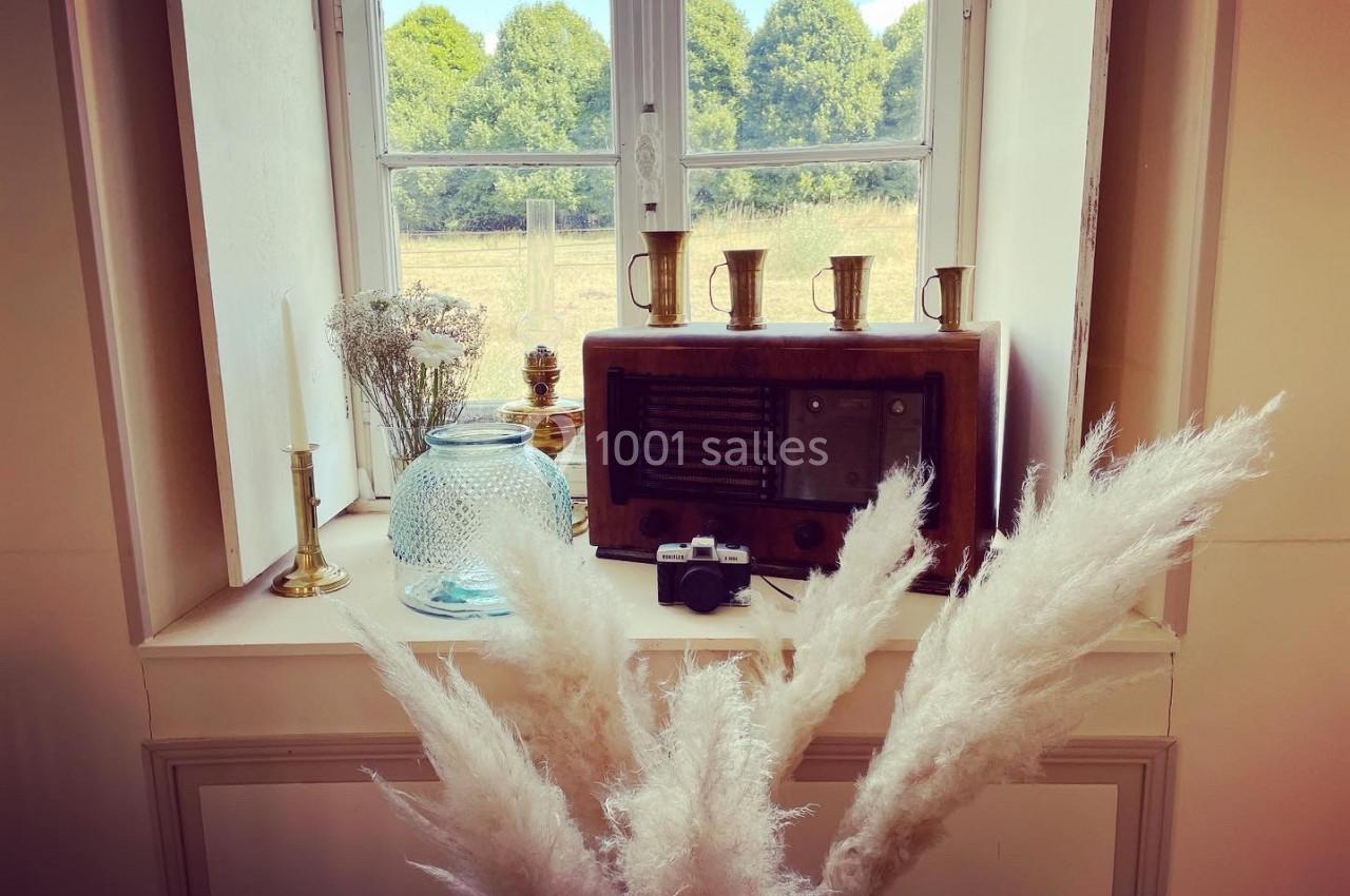 Rebord de fenêtre décoré avec une radio vintage, des vases, des bougies, une petite caméra et des herbes de la pampa.