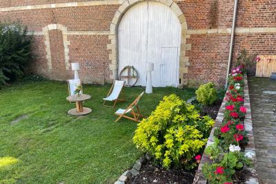 Miniature Espace détente en extérieur devant la Bergerie Pièce rustique avec murs en pierre, plafond en bois, réservoir métallique rouge et mobilier simple.
