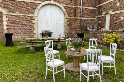 Miniature Espace extérieur devant la Bergerie Pièce rustique avec murs en pierre, plafond en bois, réservoir métallique rouge et mobilier simple.