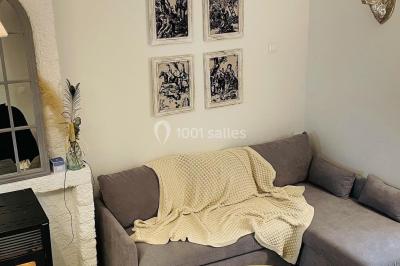 Miniature Espace salon du gîte Pièce rustique avec murs en pierre, plafond en bois, réservoir métallique rouge et mobilier simple.