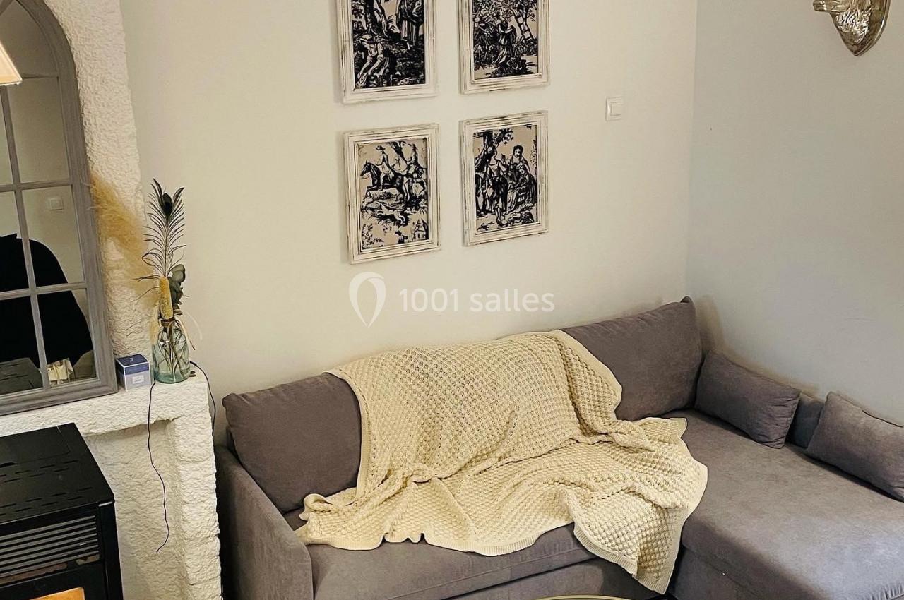 Canapé gris avec plaid beige dans un salon cosy, décoré de cadres, tête de cerf murale et table basse ronde.