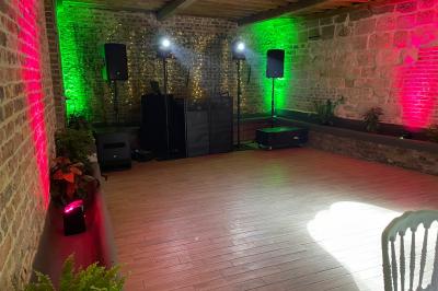 Miniature La Bergerie ( piste de danse ) Pièce rustique avec murs en pierre, plafond en bois, réservoir métallique rouge et mobilier simple.