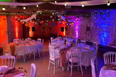 Miniature La Bergerie ( version tables rondes et piste de danse, 60 personnes ) Pièce rustique avec murs en pierre, plafond en bois, réservoir métallique rouge et mobilier simple.