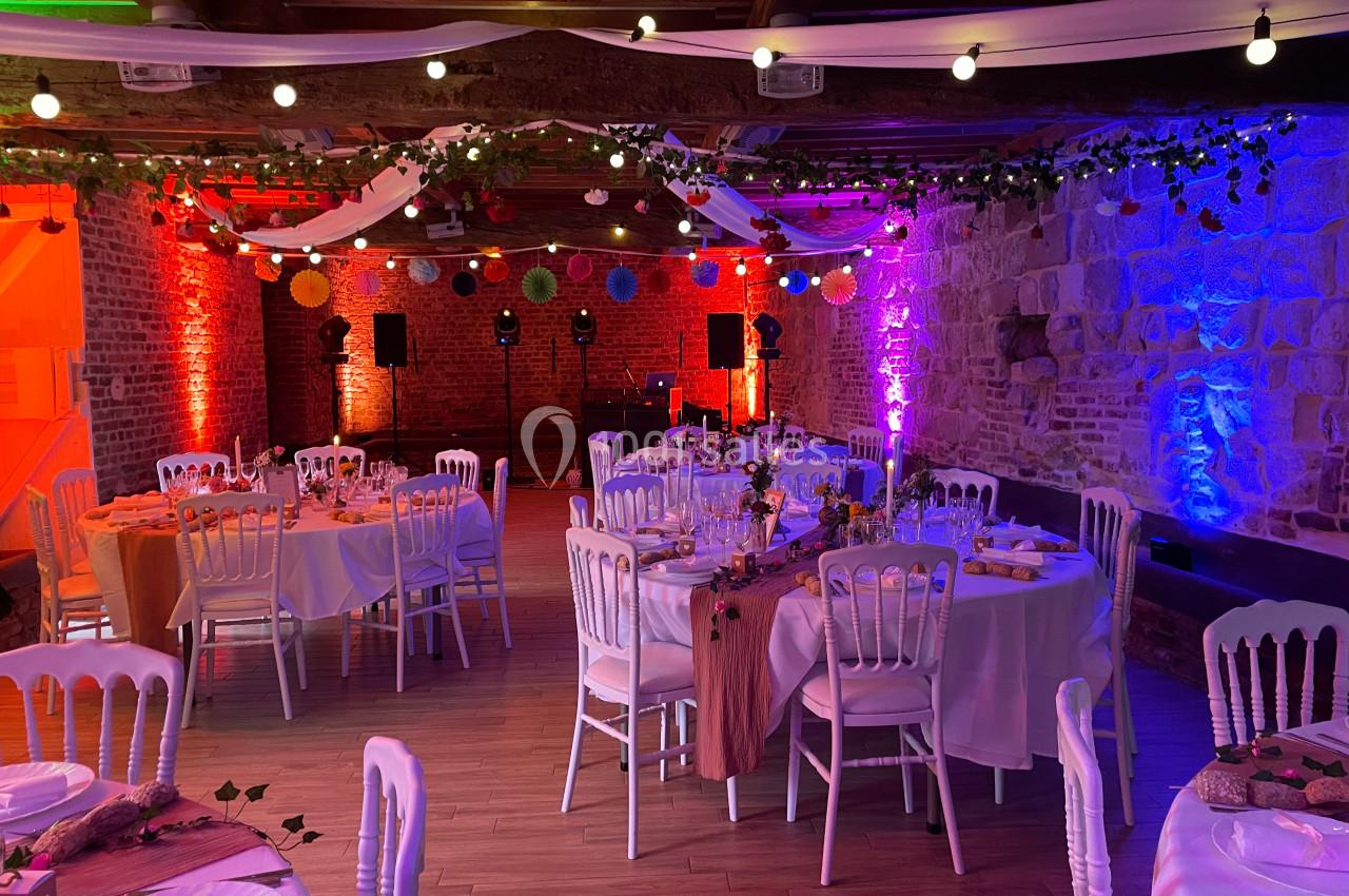 Salle de réception décorée avec des guirlandes lumineuses, tables dressées et éclairage coloré.