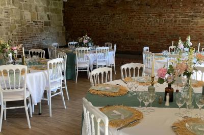 Miniature La Bergerie ( version tables rondes ) Pièce rustique avec murs en pierre, plafond en bois, réservoir métallique rouge et mobilier simple.
