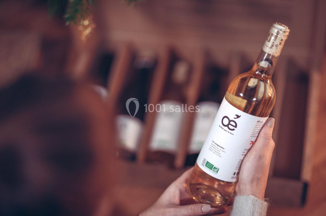 Une personne tient une bouteille de vin blanc biologique devant une caisse contenant d'autres bouteilles.