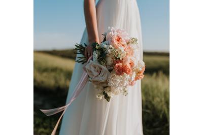 Un couple en tenue de mariage s'embrasse sous un voile, tenant un bouquet de fleurs.