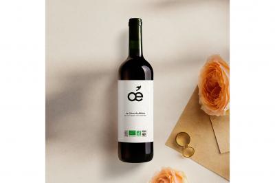 Une bouteille de vin blanc bio, un verre en cours de remplissage, des olives et des herbes sur une table jaune.