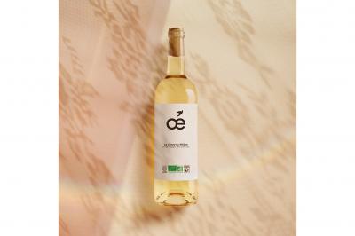 Une bouteille de vin blanc bio, un verre en cours de remplissage, des olives et des herbes sur une table jaune.