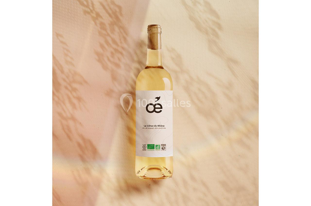 Bouteille de vin blanc bio posée sur une surface beige avec des ombres et reflets lumineux.