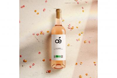 Une bouteille de vin blanc bio, un verre en cours de remplissage, des olives et des herbes sur une table jaune.