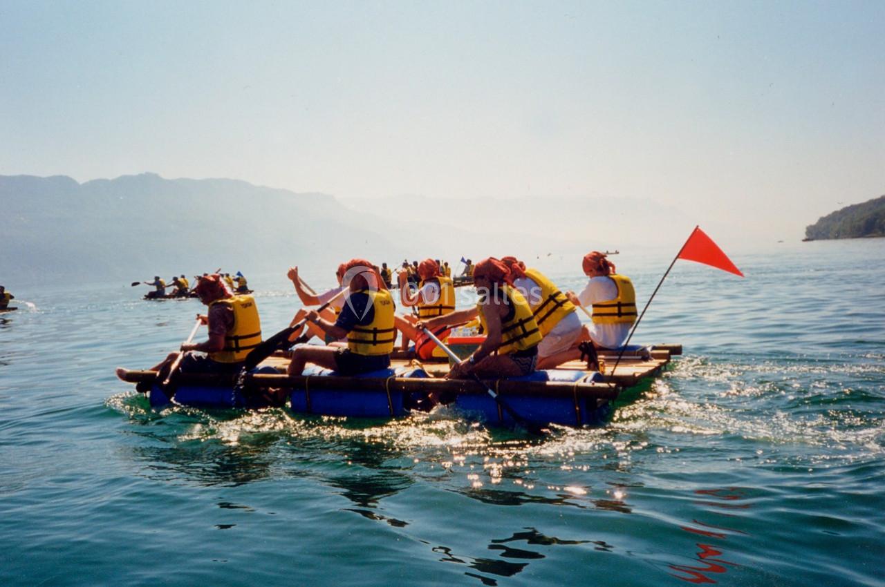 Des personnes en gilets de sauvetage pagaient sur un radeau improvisé sur un lac entouré de montagnes.