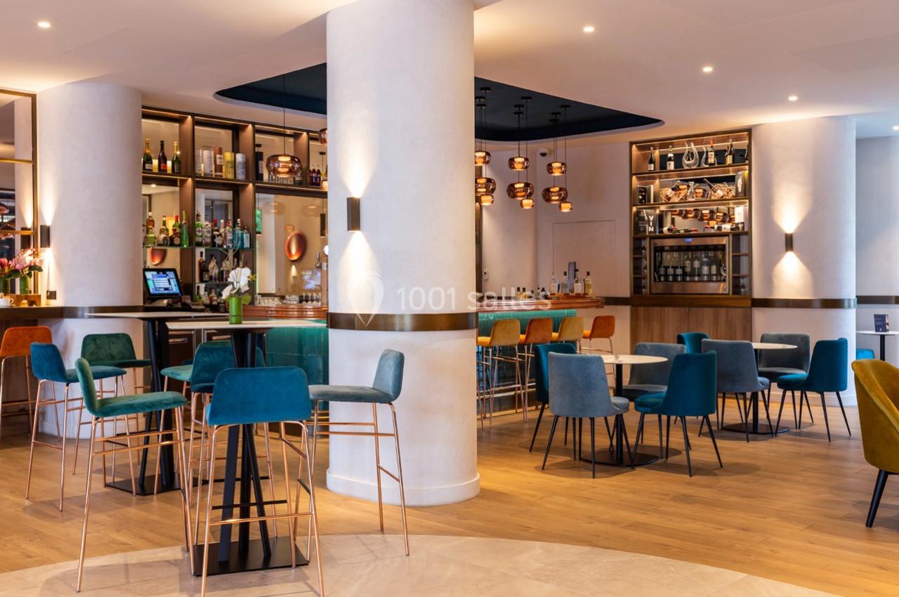 Salle de restaurant moderne avec tables, chaises colorées, bar éclairé et étagères garnies de bouteilles.
