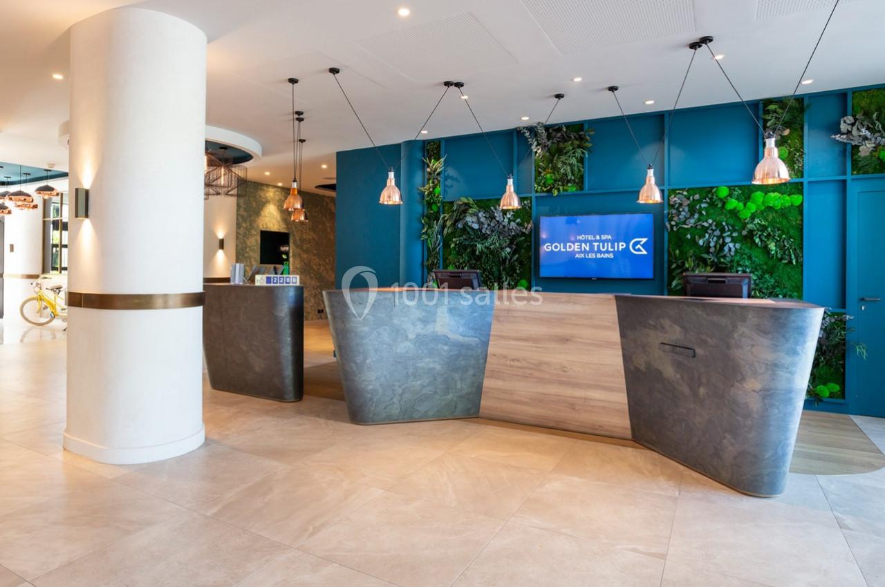 Accueil d'un hôtel moderne avec un comptoir en bois et pierre, mur végétal et éclairage suspendu.