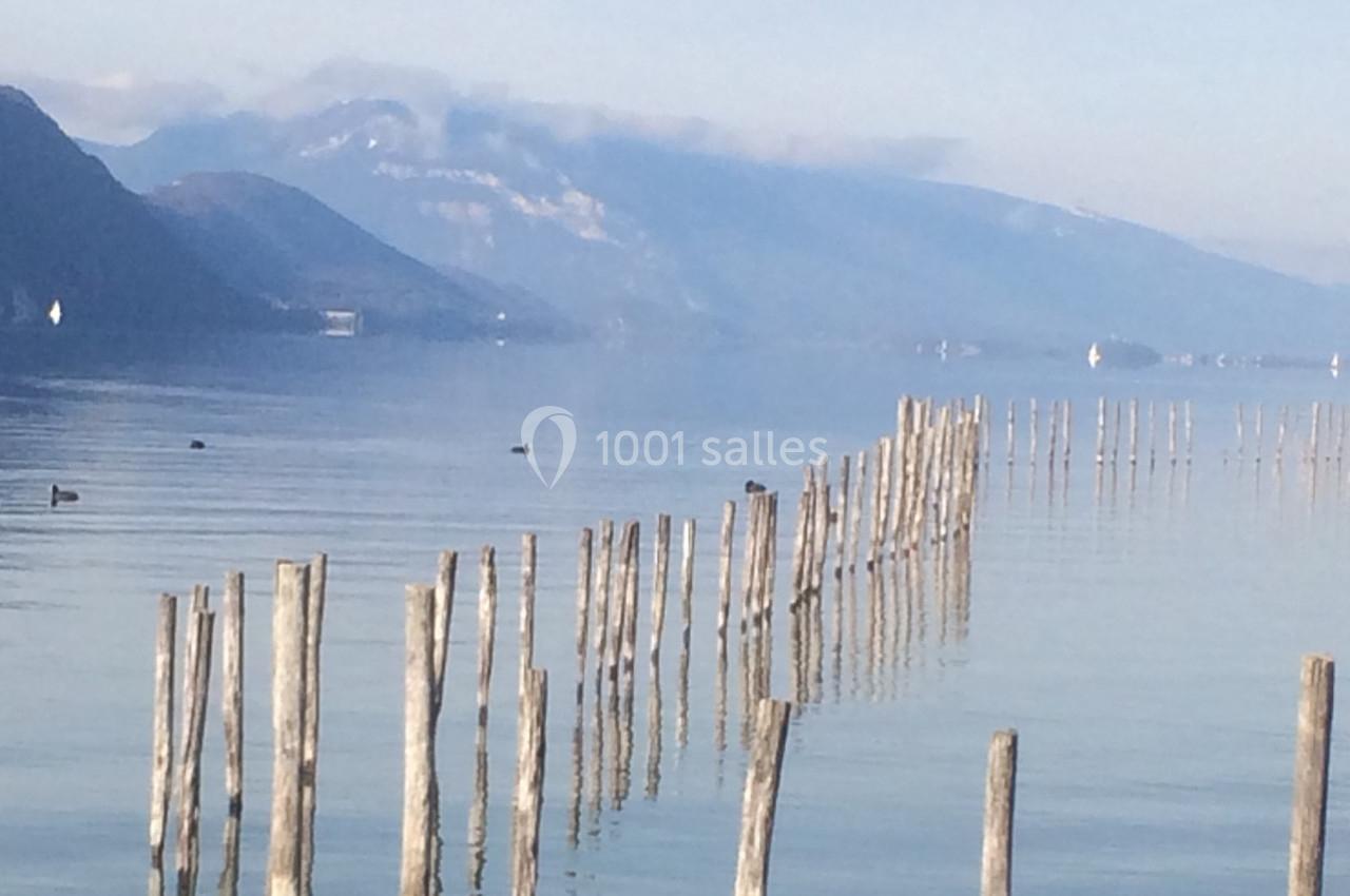 Lac calme avec montagnes en arrière-plan, rangée de poteaux en bois traversant l'eau et quelques oiseaux flottants.