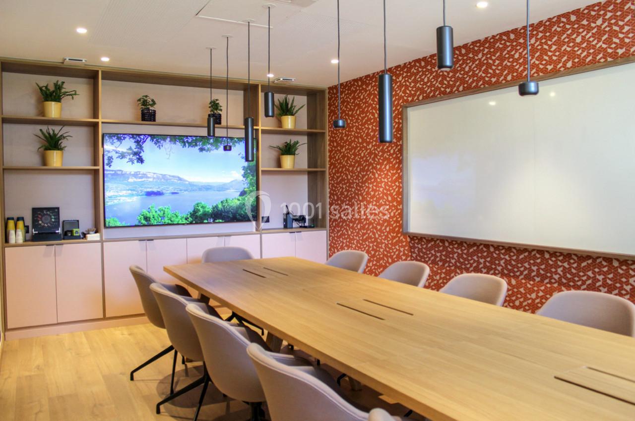 Salle de réunion moderne avec grande table en bois, écran mural, tableau blanc et étagères décorées de plantes.
