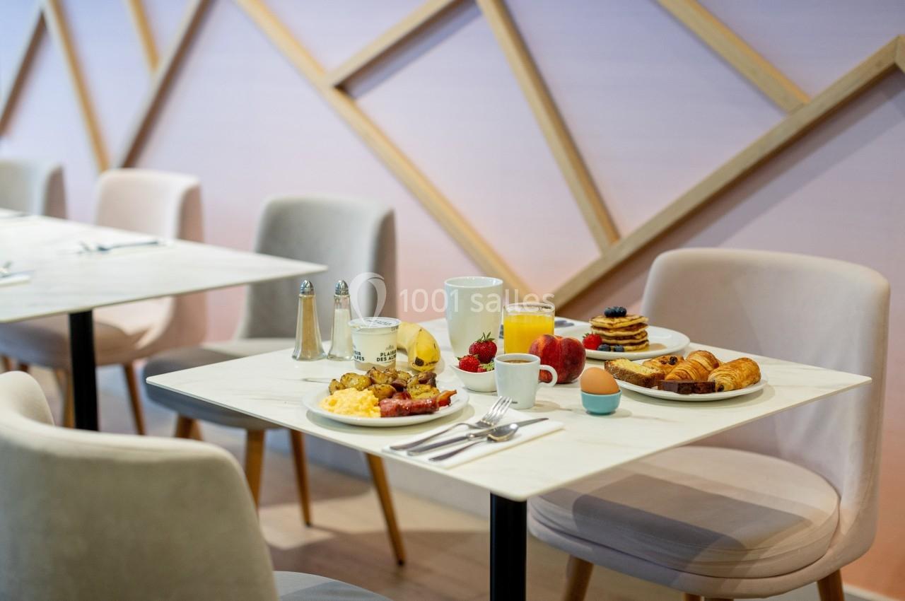 Table de petit-déjeuner avec assiettes de viennoiseries, fruits, pancakes, œufs, jus d'orange et café.