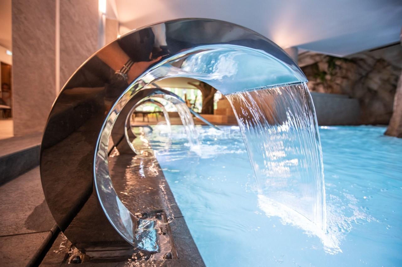 Jet d'eau courbé en acier inoxydable déversant de l'eau dans une piscine intérieure éclairée.