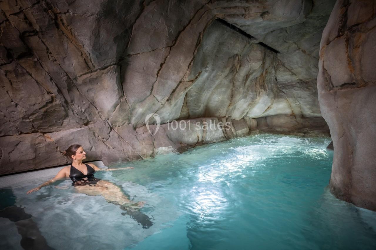 Femme en maillot de bain noir se relaxant dans une piscine naturelle entourée de parois rocheuses.