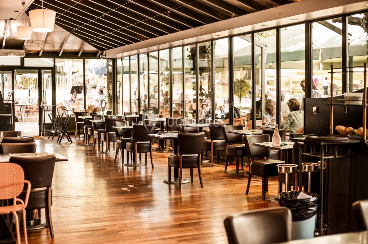 Salle de restaurant lumineuse avec des tables et chaises en bois, grandes baies vitrées donnant sur l'extérieur.