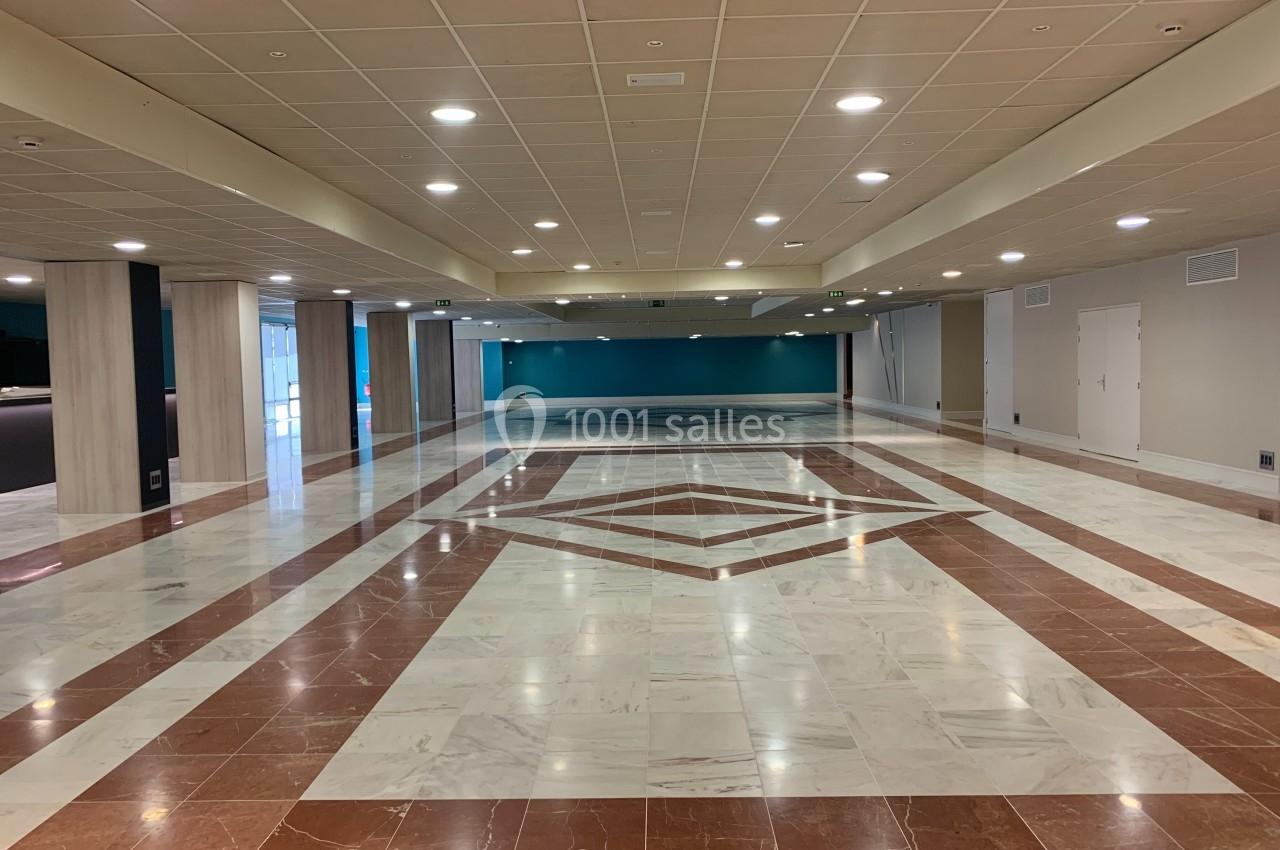 Salle spacieuse avec sol en marbre, motifs géométriques et éclairage encastré au plafond.