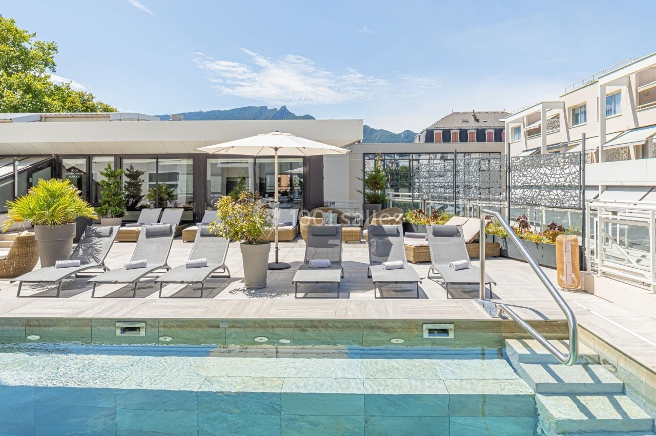 Terrasse avec piscine, transats, parasol et vue sur des montagnes sous un ciel dégagé.