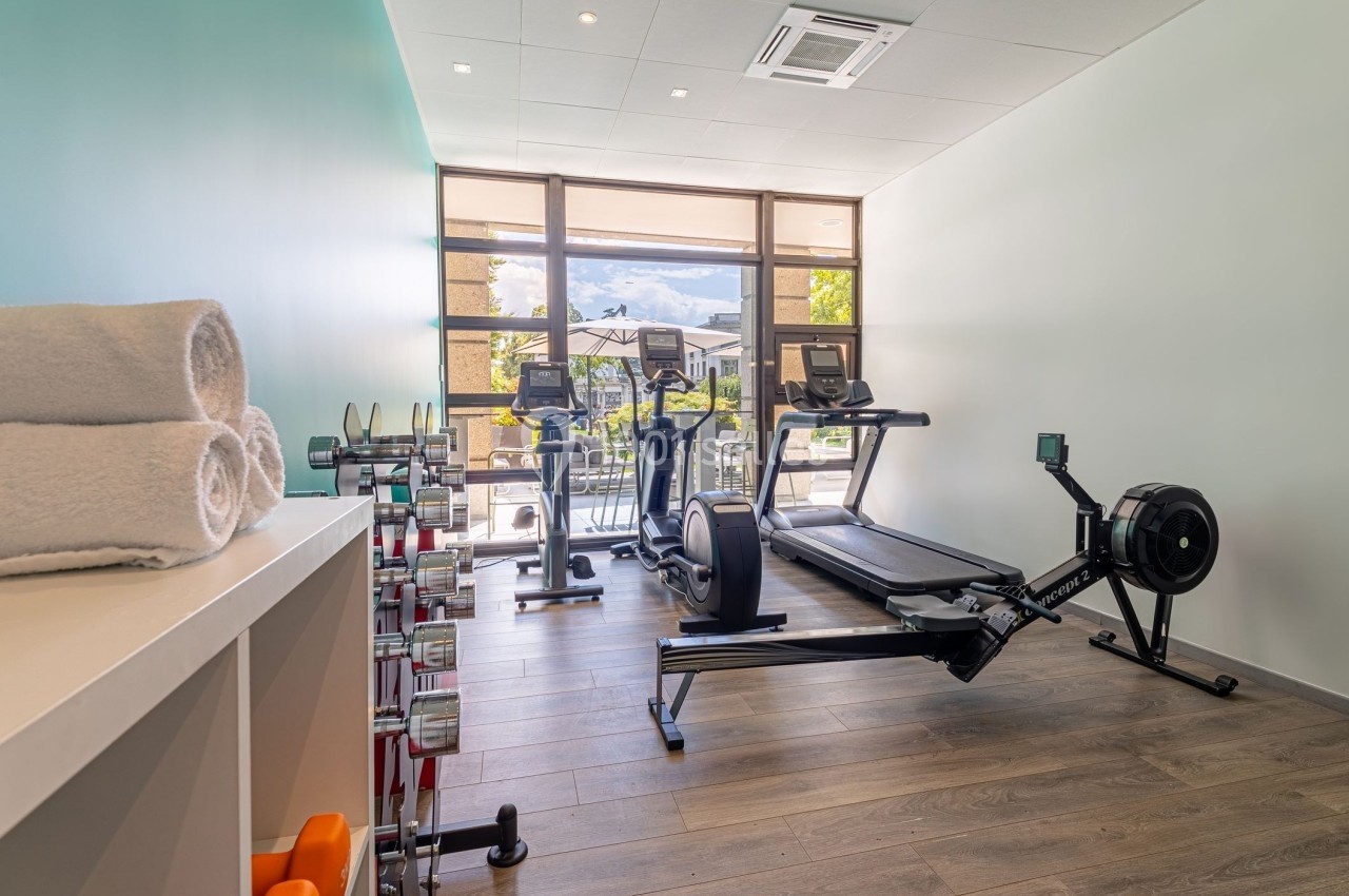 Salle de sport lumineuse avec tapis de course, rameur, haltères et serviettes pliées sur une étagère.