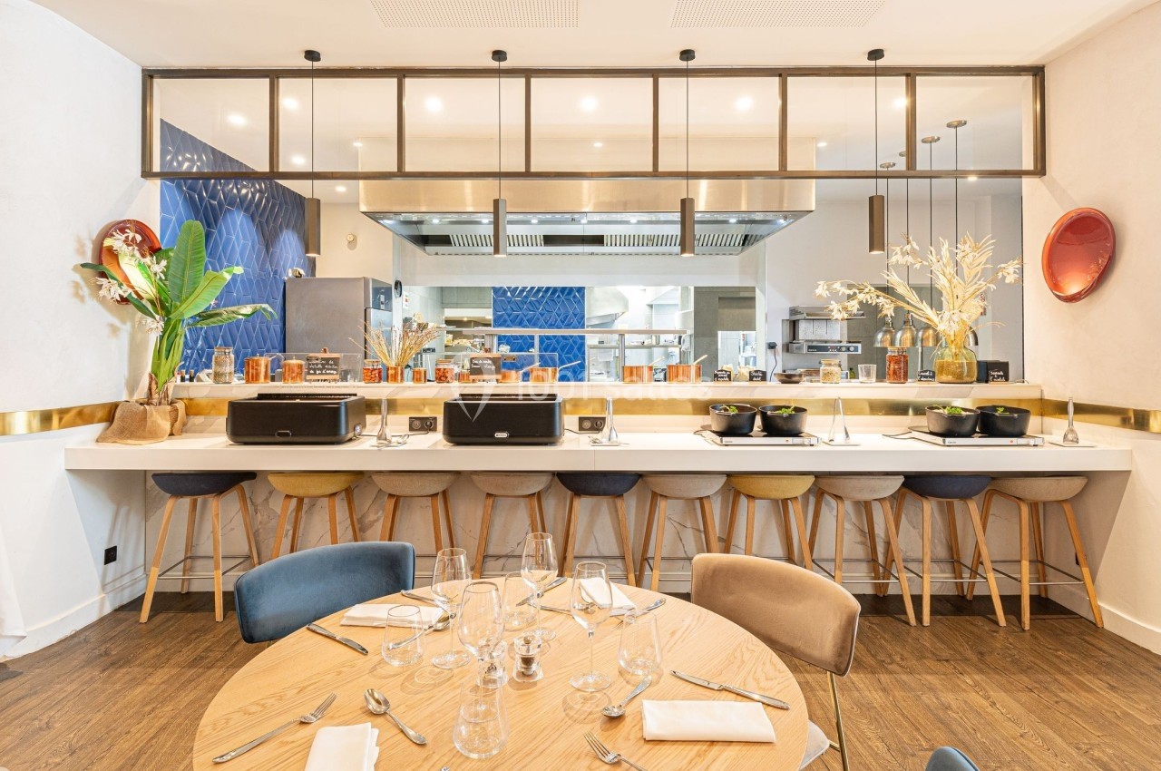 Cuisine ouverte moderne avec comptoir, tabourets colorés, table dressée et décoration lumineuse.